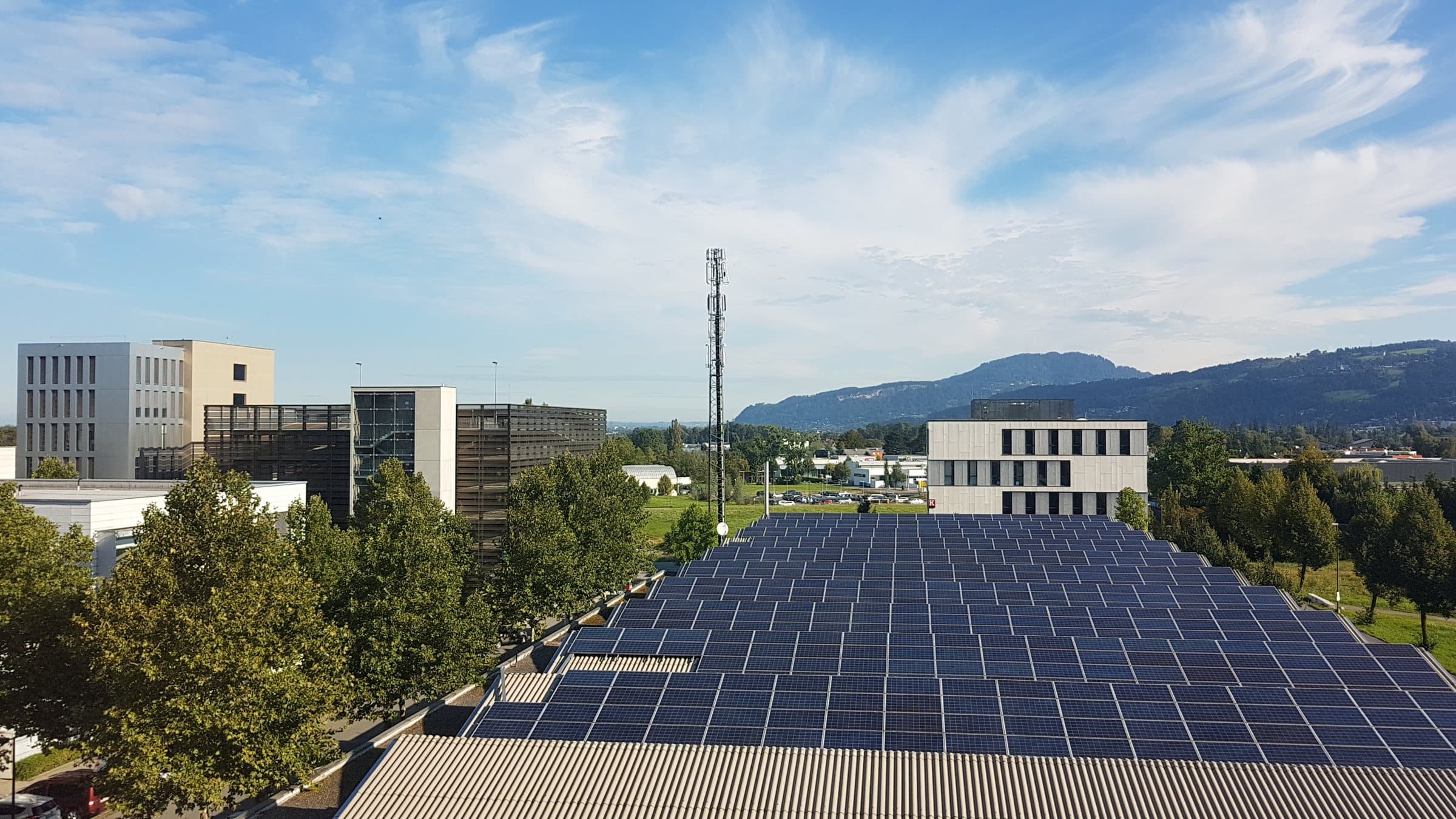 A wide solar array on the roof of a commercial building, with offices and hills behind.