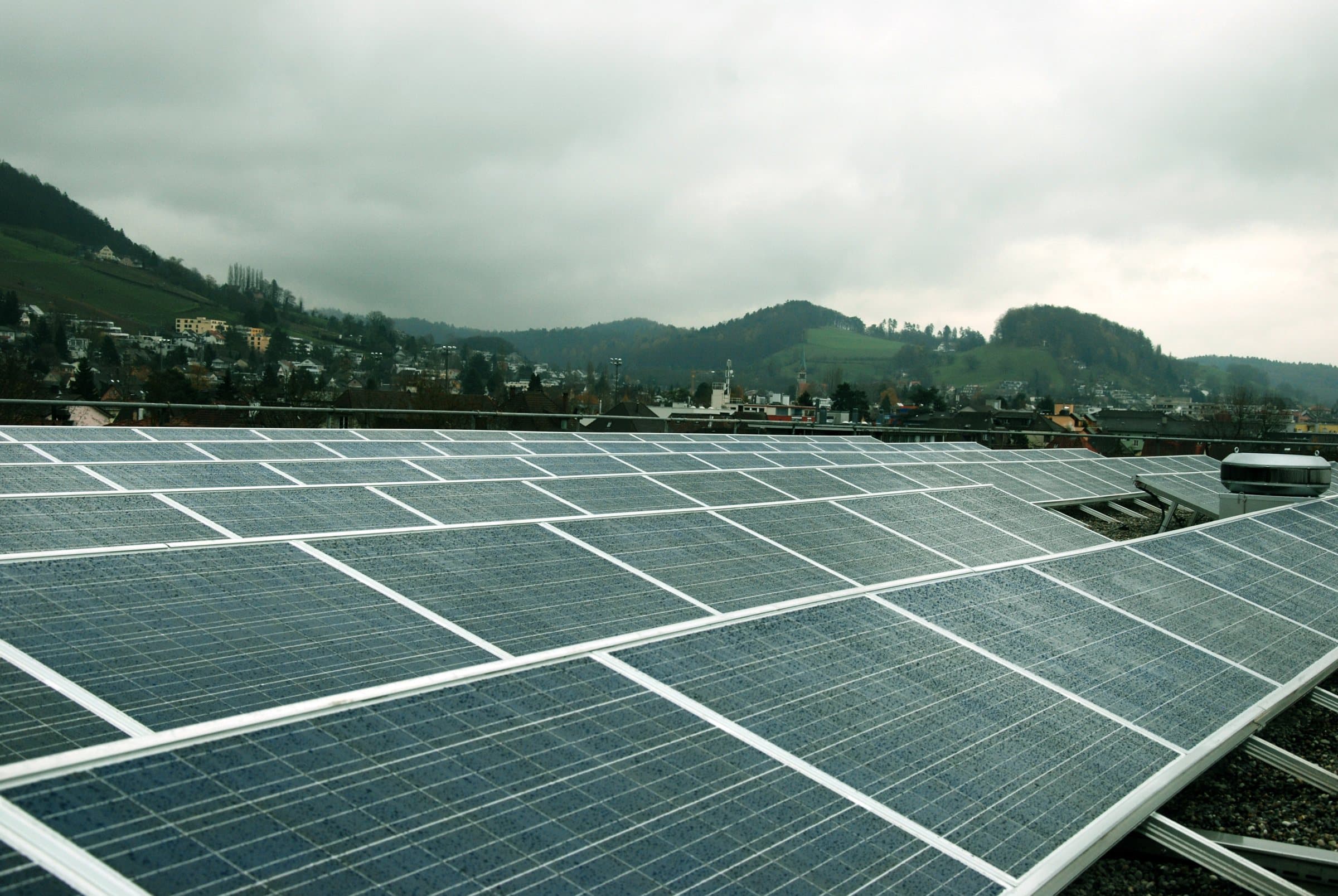 Rows of solar panels across a large flat roof, with hills in the distance.