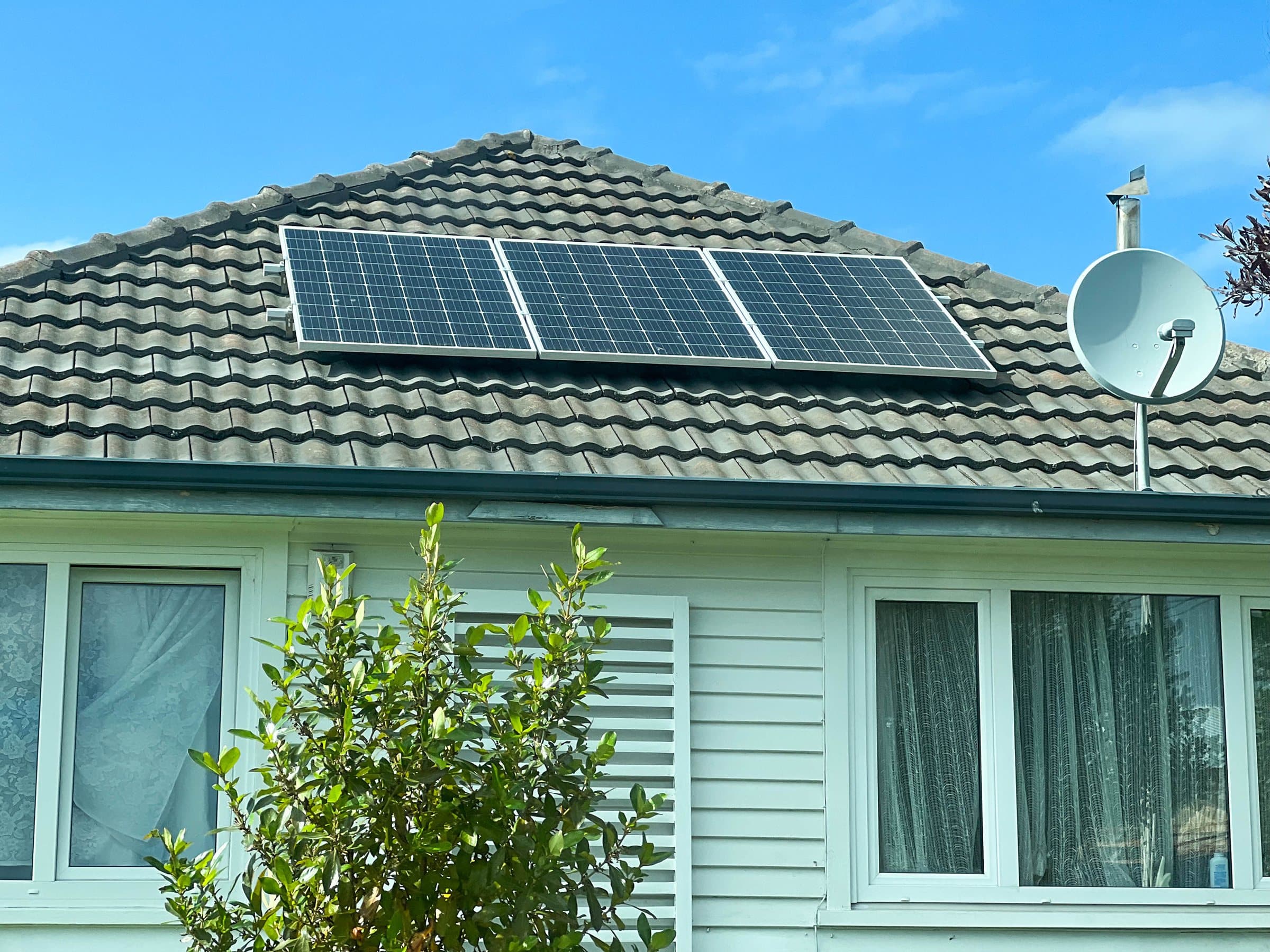 Solar panels mounted on the tiled roof of a house, seen from the garden.